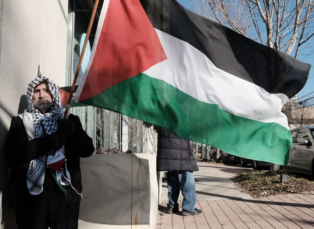 Father George Makhlouf holds a Palestinian flag as a group of protesters gather outside of the Israeli Consulate building in Atlanta.
