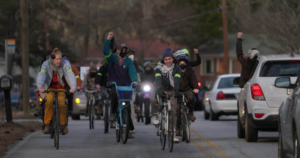 An image of multiple bikers and car drivers holding up fists during a procession in honor of Tortuguita