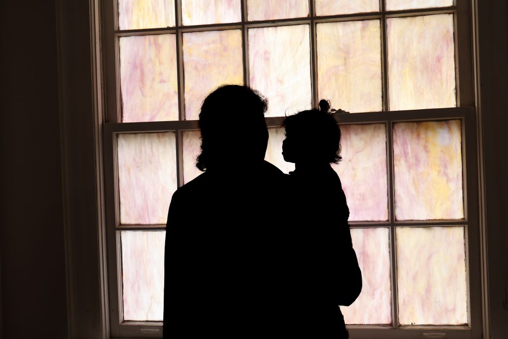 A silhouette of an asylum-seeking mother holding her daughter in front of a stained-glass window.