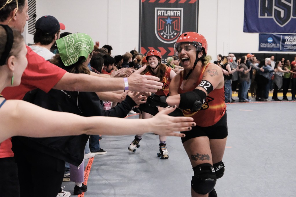 A roller derby player smiles while skating and giving high fives to fans.