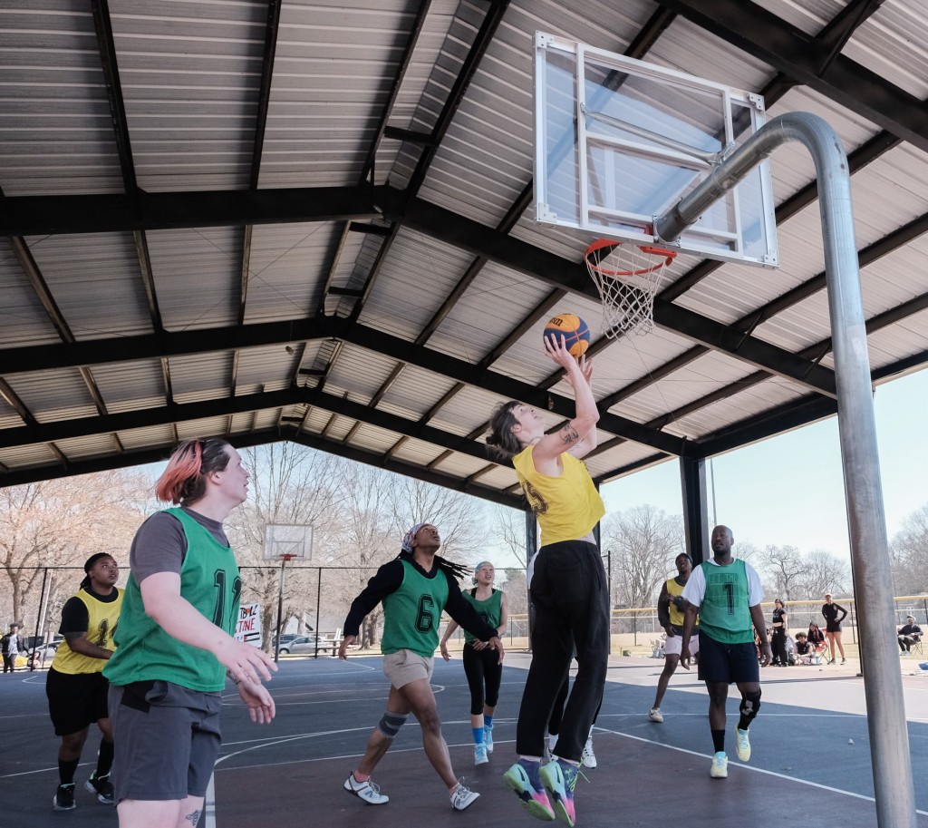 A basketball player wearing yellow goes for a shot while players wearing green watch.