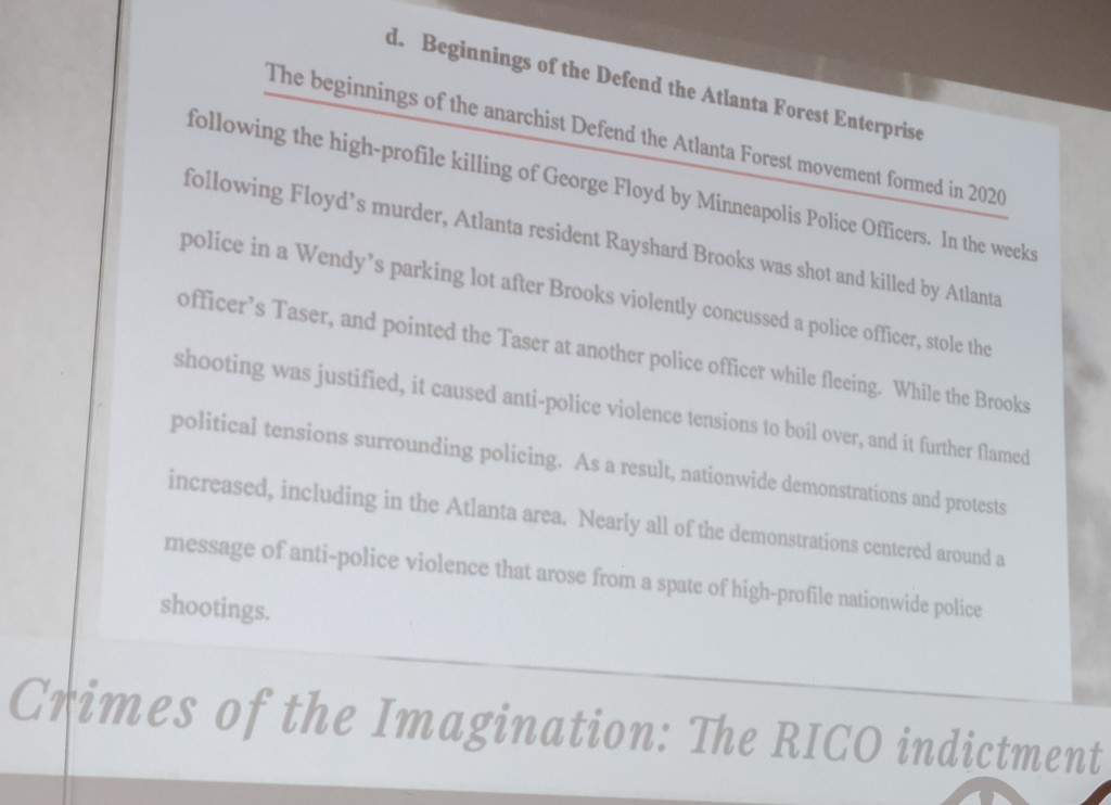 A slide shows part of the anti-racketeering indictment brought against 61 people alleged to be part of the Stop Cop City movement.