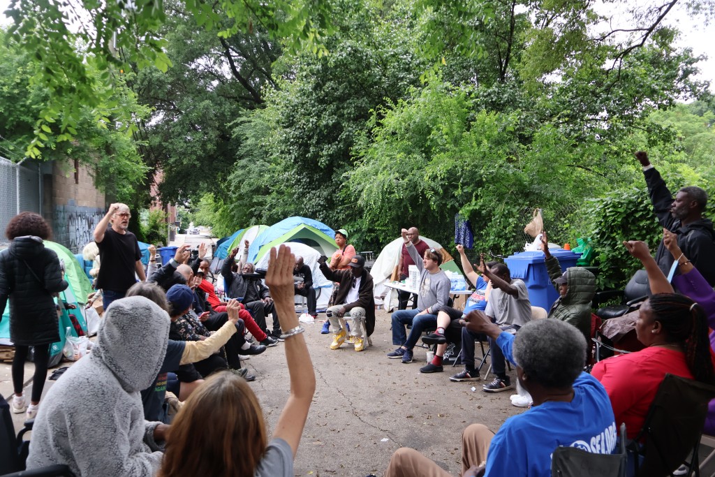 A group of people sitting in a circle on a gravel backstreet discussing housing first policy for Atlanta.