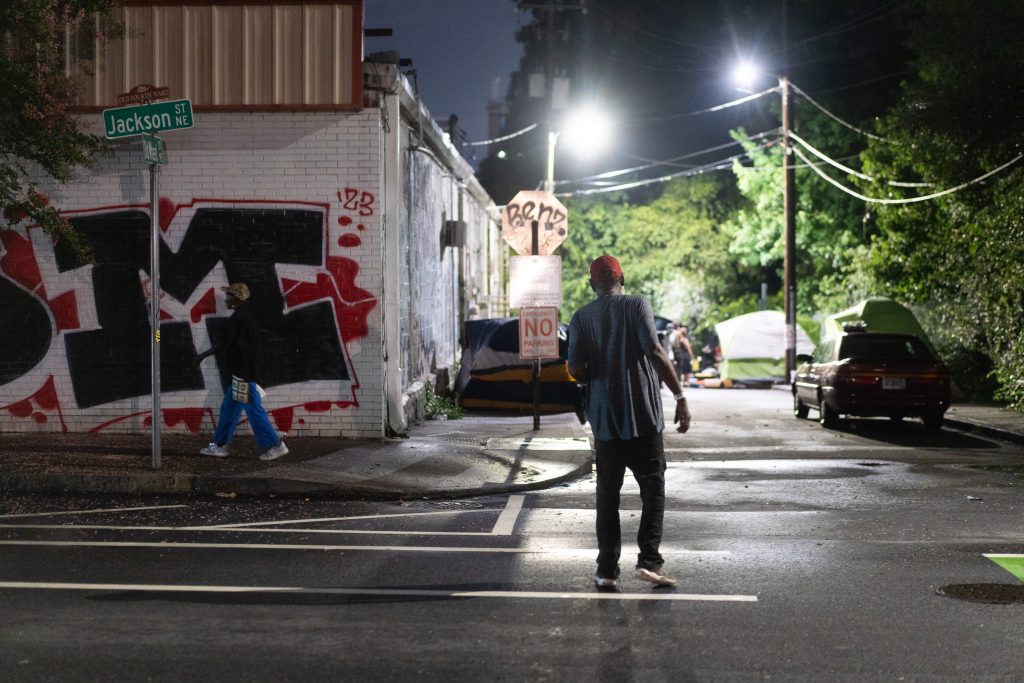A man in a red baseball cap walks towards Old Wheat St.