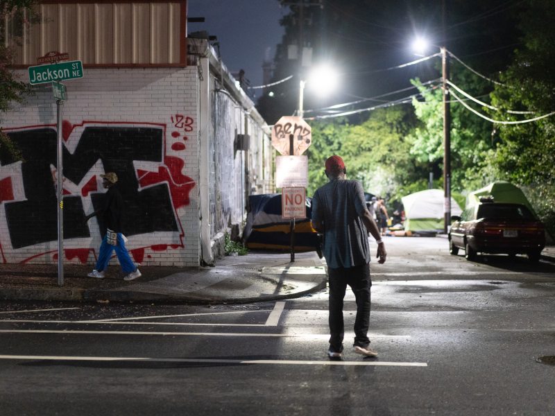 A man in a red baseball cap walks towards Old Wheat St.