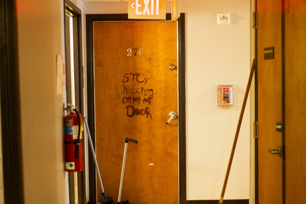 A wooden door that has "STOP knocking on my mf door" in marker written on it.