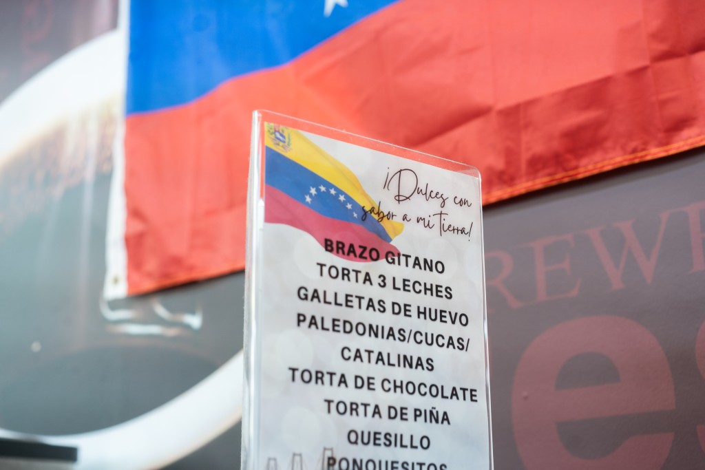 A sign on a counter in front of the Venezuelan flag that advertises "sweets with the taste of home."