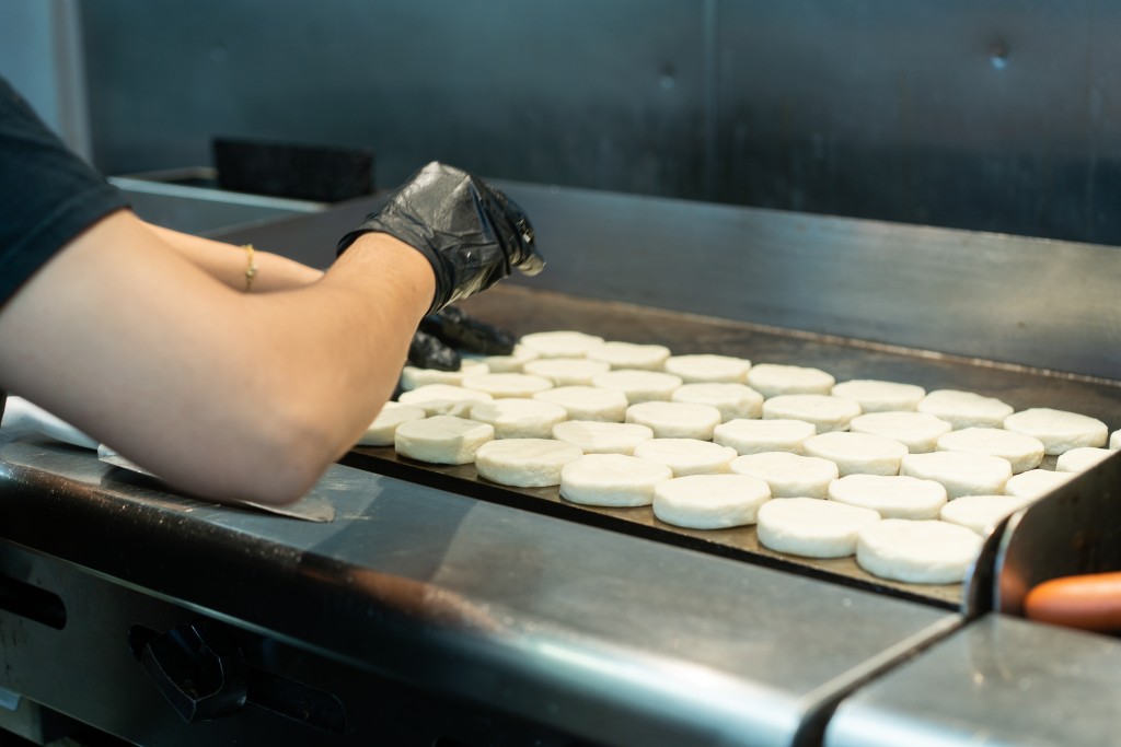 A person arranges arepas on a cooktop griddle.
