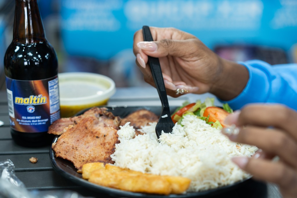 A woman eats a plate of rice, meat, and vegetables.
