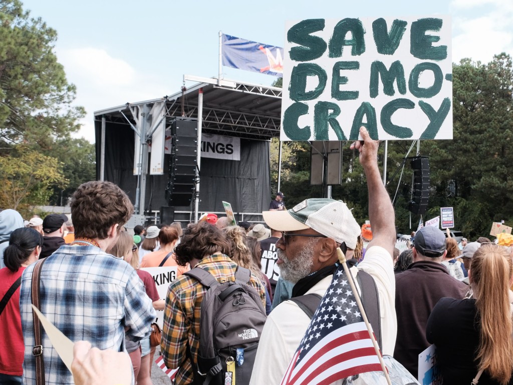 A protestor holds up a sign that reads "Save Democracy."