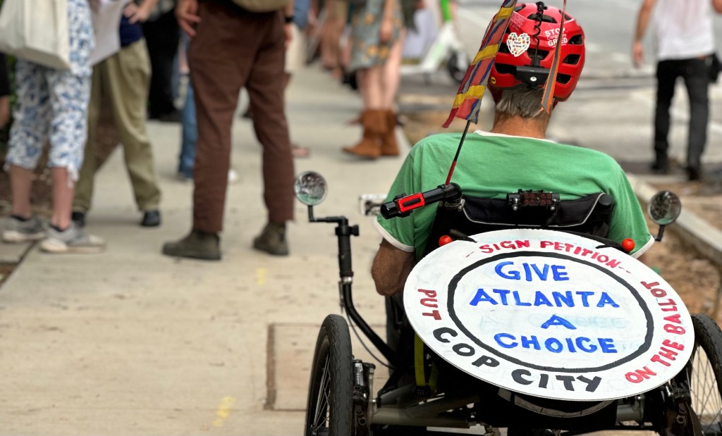 Tom Coffin rides his recumbent bike with a sign supporting the Cop City referendum at a protest in front of Home Depot in Midtown, Atlanta. (Matt Scott)