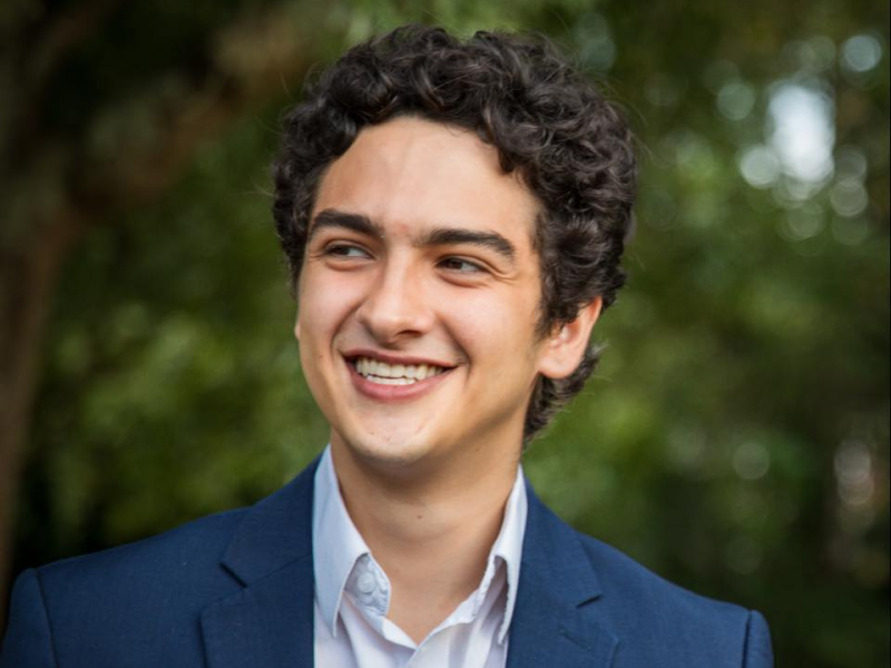A man with dark curly hair looks and smiles at something to the left of the camera.