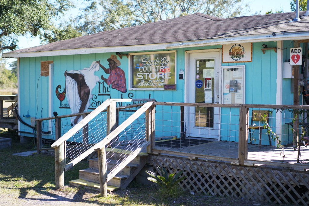 A bright blue building with paintings of two men on its side. The building's sign reads "Sapelo Country Store."
