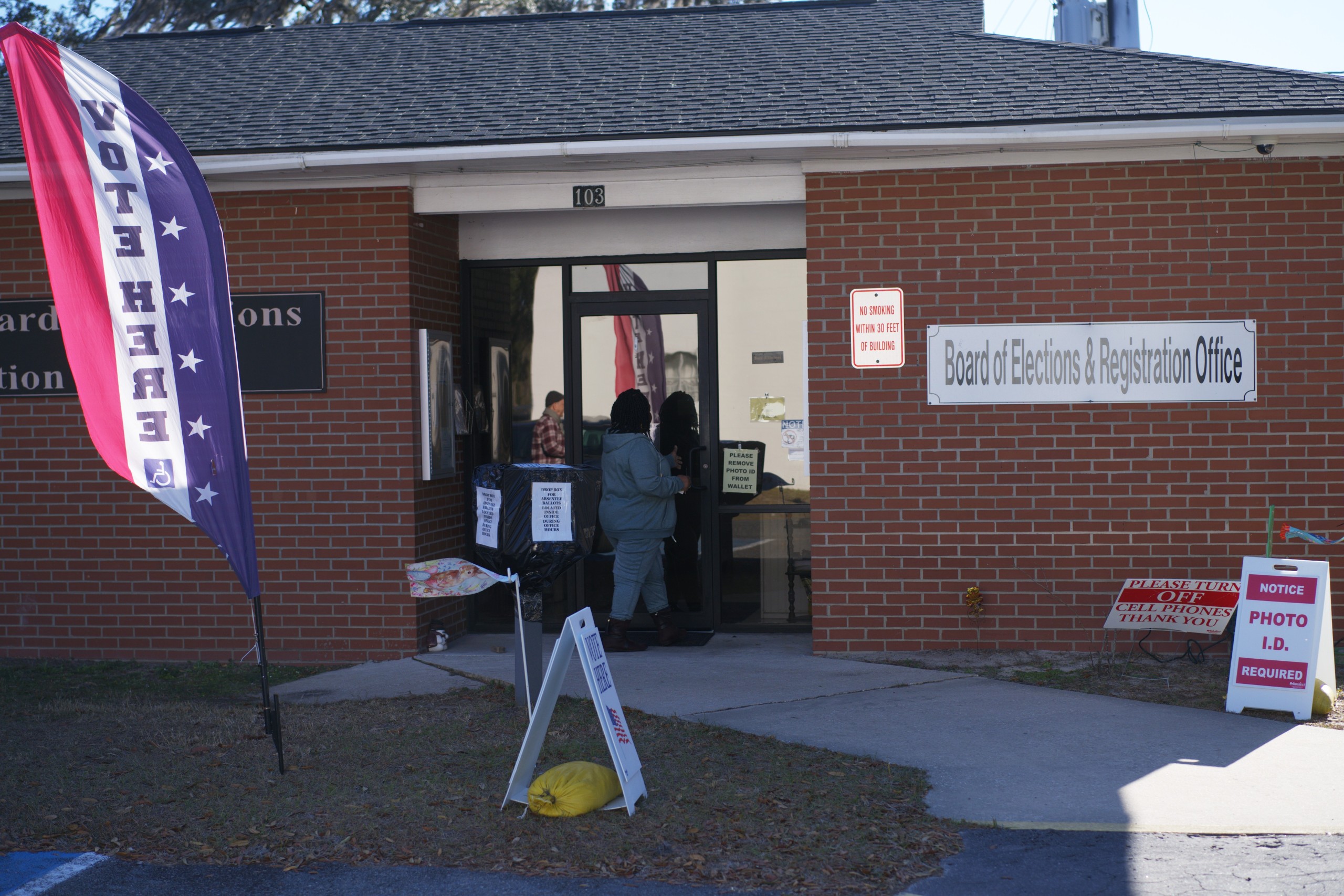 A woman walks into a brick building with a sign that reads "Board of Elections & Registration Office."