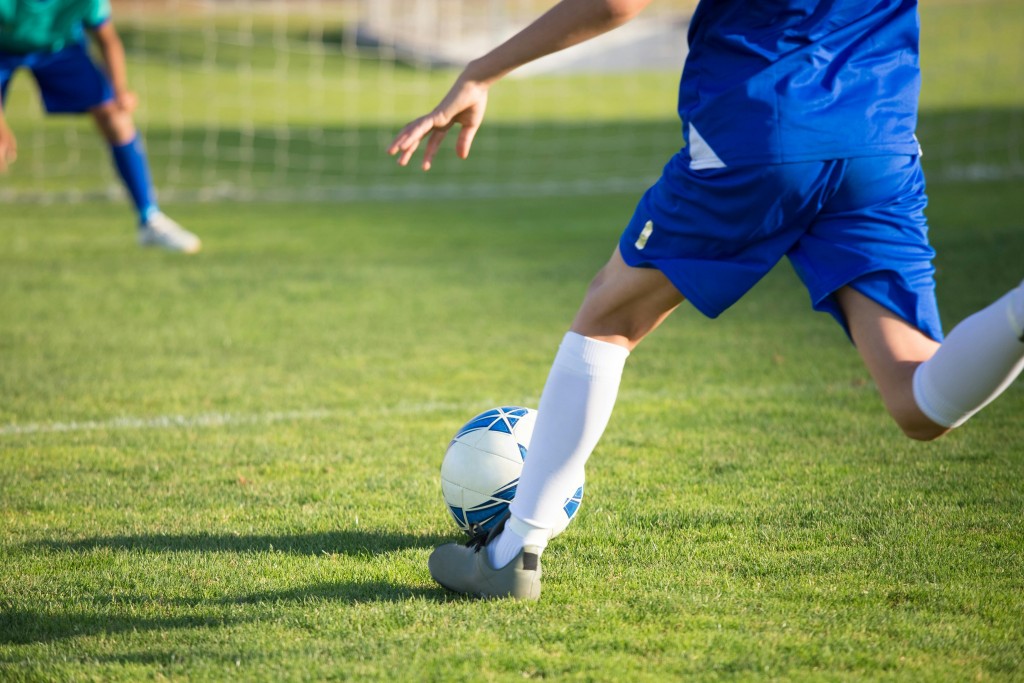 A man wearing a blue soccer uniform gets ready to kick a soccer ball into the opposing team's goal.