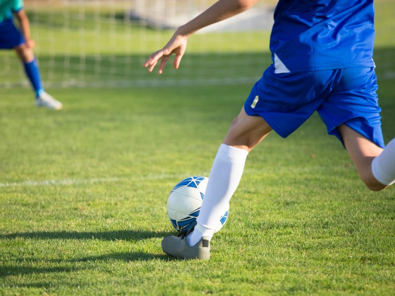 A man wearing a blue soccer uniform gets ready to kick a soccer ball into the opposing team's goal.