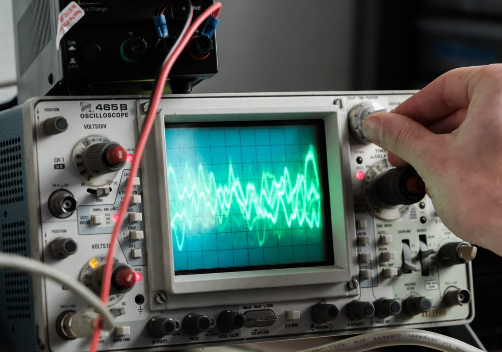 A hand adjusts a dial on an oscilloscope