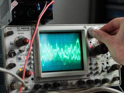 A hand adjusts a dial on an oscilloscope
