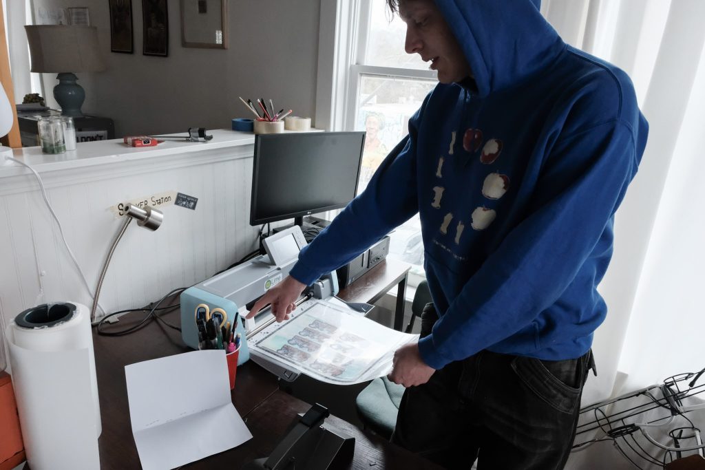 A person wearing a blue hoodie points at a scan-and-cut machine.