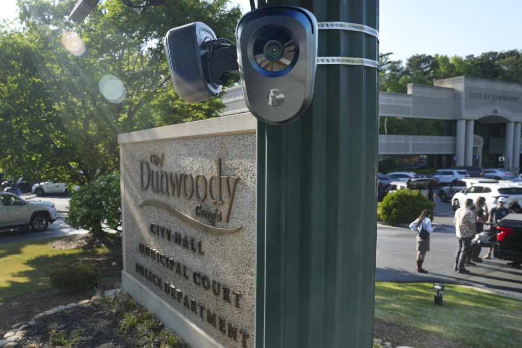 Two Flock Safety cameras hang in front of the sign for Dunwoody City Hall. 